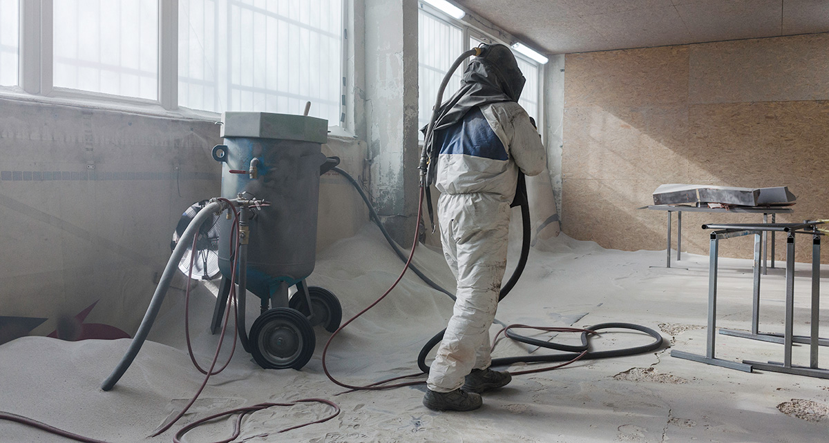 Worker in protective equipment using industrial sandblasting equipment